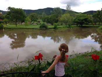 Rear view of girl standing by lake against sky