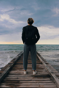 Rear view of man standing on pier over sea against sky