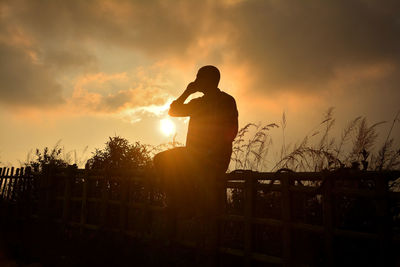 Silhouette man standing by railing against cloudy sky during sunset