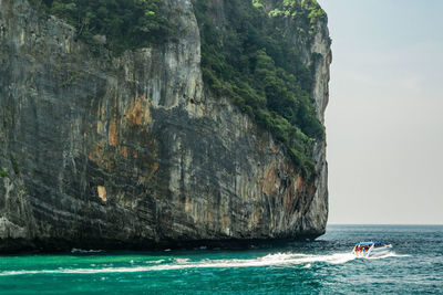 Yacht sailing on sea by rocky mountain against sky