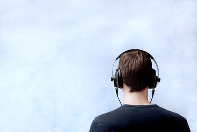 Rear view of young man listening music while standing against cloudy sky