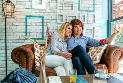 Man taking selfie with girlfriend from mobile phone while sitting on sofa