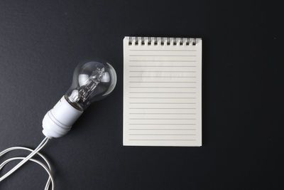 High angle view of light bulb by note pad against black background