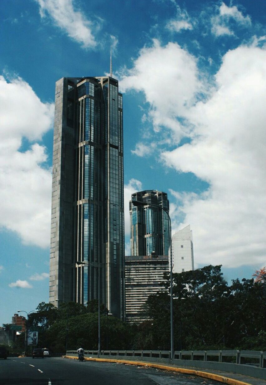 building exterior, architecture, built structure, sky, cloud - sky, city, street, road, low angle view, transportation, cloud, building, car, tower, cloudy, modern, office building, tall - high, land vehicle, day