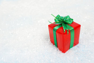 Christmas red gift box with green bow on white snow background