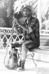 Portrait of man holding guitar while sitting on bench