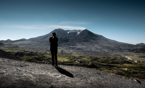 Rear view of silhouette man standing on mountain against sky