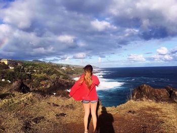 Rear view of young woman standing on beach against sky