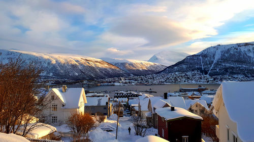 Snow covered houses by buildings against sky