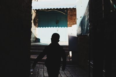 Rear view of silhouette boy walking on footpath against building