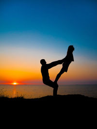 Silhouette couple exercising at beach against sky during sunset
