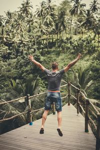 Rear view of man jumping on railing against trees