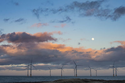 Wind turbines in sea against sky during sunset