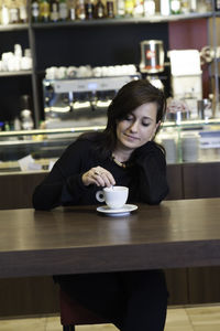 Young woman stirring coffee while sitting at table in cafe