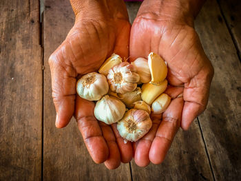 Directly above shot of person holding garlic bulbs and cloves over wooden table