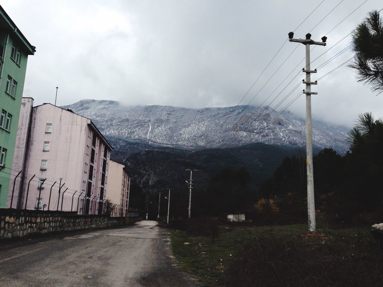 mountain, sky, the way forward, road, street light, cloud - sky, snow, weather, transportation, building exterior, cold temperature, street, mountain range, built structure, winter, architecture, electricity pylon, nature, diminishing perspective, season