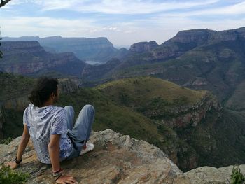 Man sitting on rock against sky