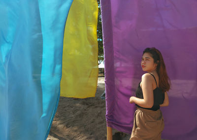 Portrait of young woman standing against fabric