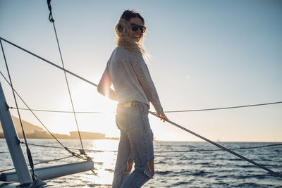 Low angle view of young woman fishing in sea against clear sky