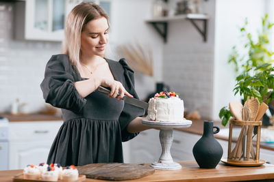 Young woman cutting cake at kitchen