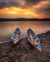 Boat moored on shore against sky during sunset