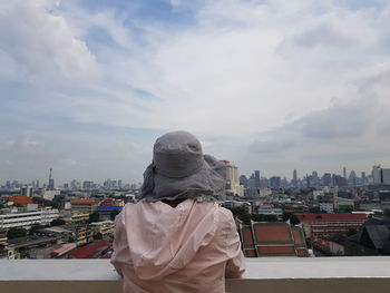 Rear view of woman wearing hat while looking at city buildings against sky