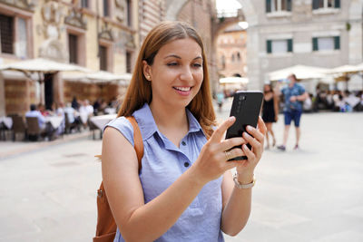 Portrait of smiling young man using smart phone on street