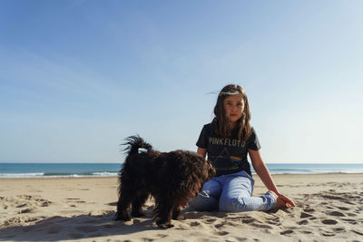 Side view of girl sitting  at beach and playing with dog