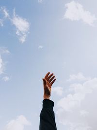 Cropped hand gesturing against blue sky