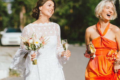 Smiling friends holding wine and bouquet on road