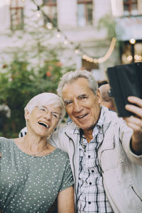 Senior man taking selfie with happy woman while sitting at restaurant in city