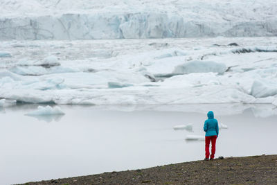 Tourist admiring the floating icebergs, fjallsarlon glacier lagoon, iceland. global warming concept