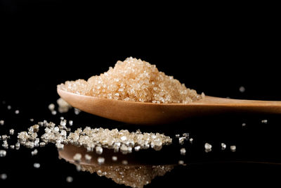 Close-up of brown sugar in wooden spoon against black background