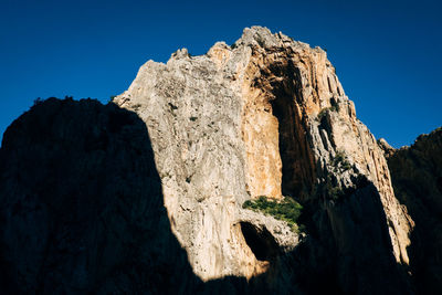 Low angle view of rock formation against clear blue sky