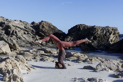 Low section of woman sitting on rock against sky