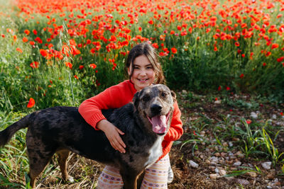 Portrait of girl in red sweater hugging her dog in the field of poppies