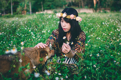 Woman wearing flowers while sitting with dog on field 