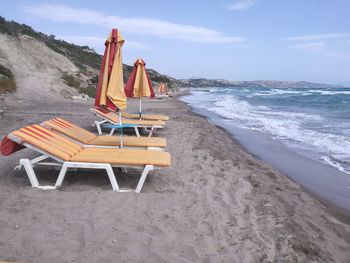 Chairs on beach by sea against sky