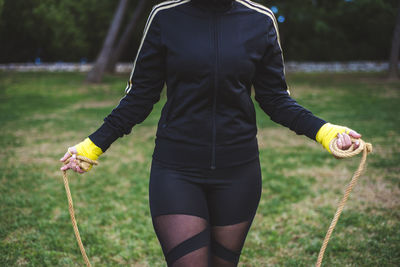 Midsection of woman holding jump rope on grass