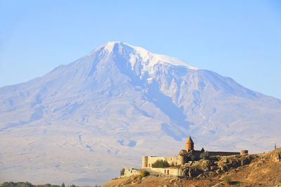 Scenic view of built structure against snowcapped mountain and sky