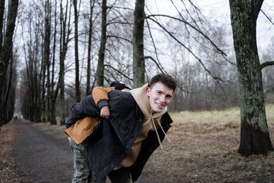 Portrait of man carrying boy on back while standing in forest