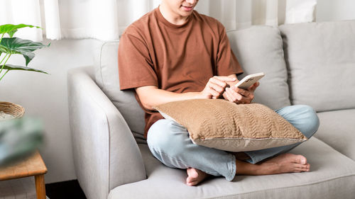 Midsection of man using smart phone on sofa