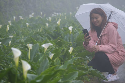 Woman photographing flowers while crouching during rainy season