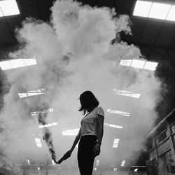 Woman holding distress flare while standing against ceiling