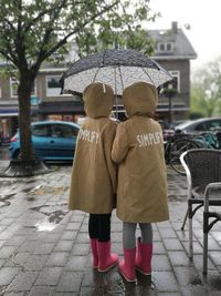 Rear view of friends with umbrella standing on footpath