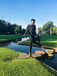 Full length of young man walking on rocks in lake against clear sky