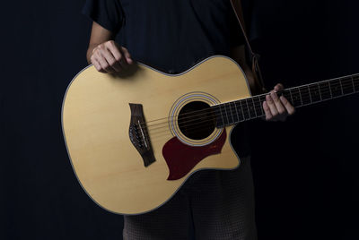 Midsection of man playing guitar against black background