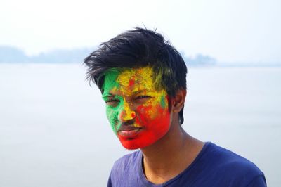Portrait of man with colorful powder paint against lake during holi