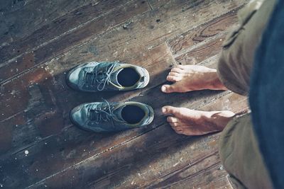 Low section of man standing by shoes on hardwood floor