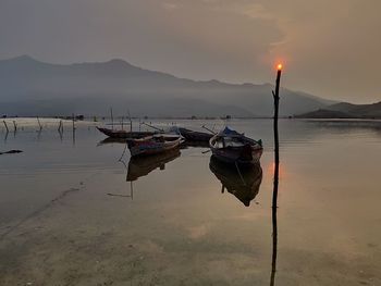 Fishing boat on lake against sky during sunset